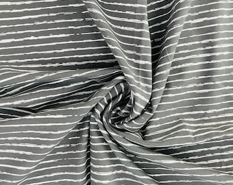 May include: Gray fabric with white horizontal brushstroke stripes. The fabric is draped and folded, creating a textured appearance. The stripes have a slightly uneven, hand-painted look, adding visual interest to the textile.