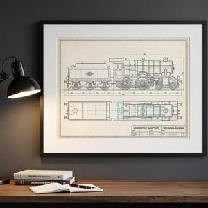 Op de afbeelding: Ingelijste kunstprint met locomotiefblauwdruk. De print toont een gedetailleerd technisch schema van een stoomtrein in blauwe lijnen op een beige achtergrond. De print zit in een zwart frame en wordt tentoongesteld op een houten bureau.