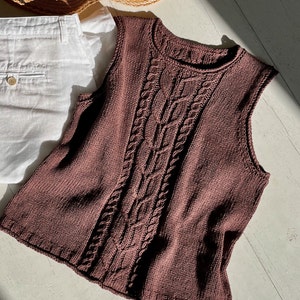 Op de afbeelding: Een bruine, mouwloze gebreide trui met een kabelbreipatroon.