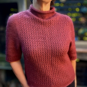 Peut inclure: Gros plan d'une femme portant un pull en tricot marron avec un col montant et des manches courtes.