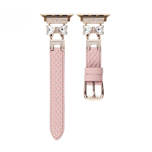 May include: A pink leather Apple Watch band with a gold buckle and two crystal bow embellishments.
