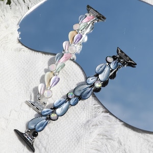 May include: Two Apple Watch bands with a leaf design. One band is silver with pastel pink, blue, and yellow leaves. The other band is black with blue leaves.