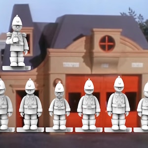 May include: A group of white toy figurines of uniformed figures, resembling firefighters, stand in front of a building with red doors and the text "THORNTON FIRE STATION". One figure is elevated above the others.