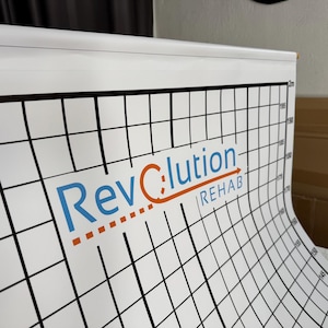 Pode incluir: Gráfico de medição branco com linhas de grade pretas e marcações de altura em centímetros. O gráfico apresenta o texto "RevClution REHAB" em azul e laranja. O gráfico está enrolado.