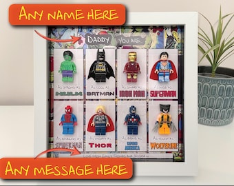 May include: A framed artwork featuring Lego superhero figures, including Hulk, Batman, Iron Man, and Superman. Each figure is paired with a descriptive phrase. The top and bottom of the frame have text that reads "Any Name Here" and "Any Message Here".