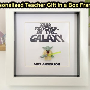 May include: A white box frame with a personalized teacher gift. The framed print features the text "YODA BEST TEACHER IN THE GALAXY" and "MRS ANDERSON". A Yoda Lego figure with a green lightsaber is in the frame.