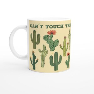 May include: White ceramic mug with a yellow background and a pattern of green cacti and orange flowers. The text "Can't Touch This" is printed in brown letters on the mug.