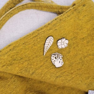 May include: Three wooden pins with a leaf, a flower, and a potted plant design. The pins are on a yellow fuzzy surface.