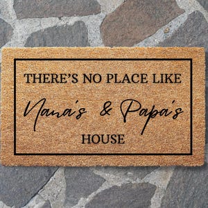 May include: A rectangular doormat with a brown coir surface and a black border. The text "THERE'S NO PLACE LIKE Nana's & Papa's HOUSE" is printed in black, creating a welcoming entrance for a home.