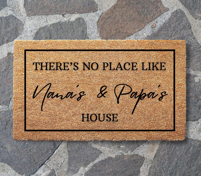 May include: A rectangular doormat with a brown coir surface and a black border. The text "THERE'S NO PLACE LIKE Nana's & Papa's HOUSE" is printed in black, creating a welcoming entrance for a home.