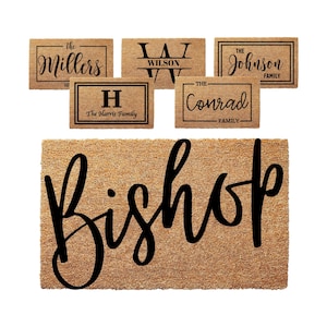 May include: A brown coir doormat with the word "Bishop" written in black cursive script. There are several smaller doormats with various family names and initials on them.