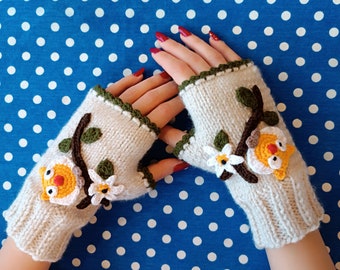May include: A pair of beige fingerless gloves with crocheted owl and flower embellishments. The gloves have a green trim and are shown against a blue polka dot background.