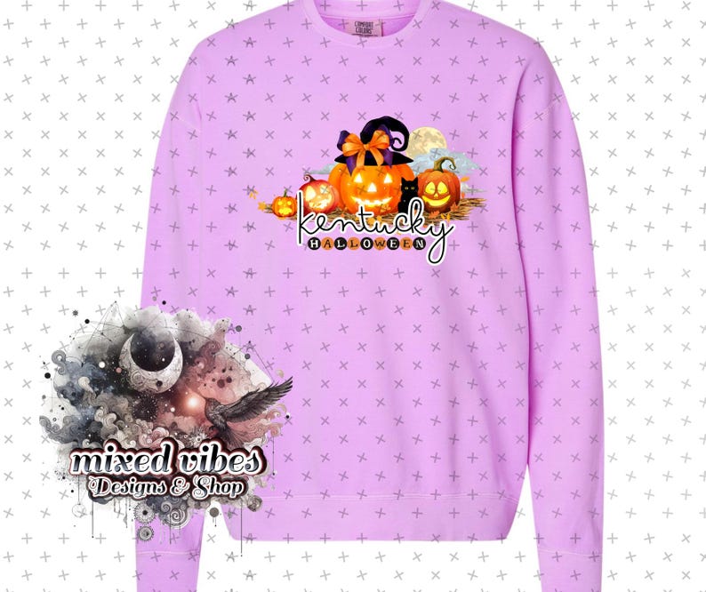 May include: A lavender sweatshirt with a graphic of pumpkins, a witch's hat, and a black cat. The text "Kentucky Halloween" is printed below the graphic. The sweatshirt has a crew neck and long sleeves.