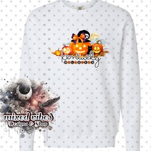 May include: White long-sleeved sweatshirt with a graphic design of pumpkins and a witch's hat. The text "Kentucky Halloween" is written below the pumpkins. The design is in orange, black, and brown colors. The sweatshirt is on a white background with a small design of a moon and a bird in the bottom left corner. The text "mixed vibes Designs & Shop" is written below the moon and bird.