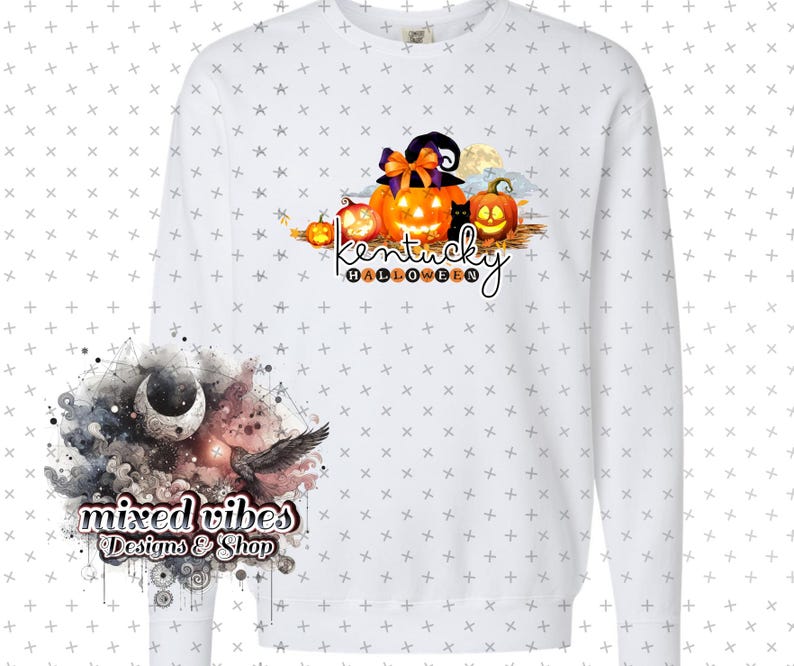 May include: White long-sleeved sweatshirt with a graphic design of pumpkins and a witch's hat. The text "Kentucky Halloween" is written below the pumpkins. The design is in orange, black, and brown colors. The sweatshirt is on a white background with a small design of a moon and a bird in the bottom left corner. The text "mixed vibes Designs & Shop" is written below the moon and bird.