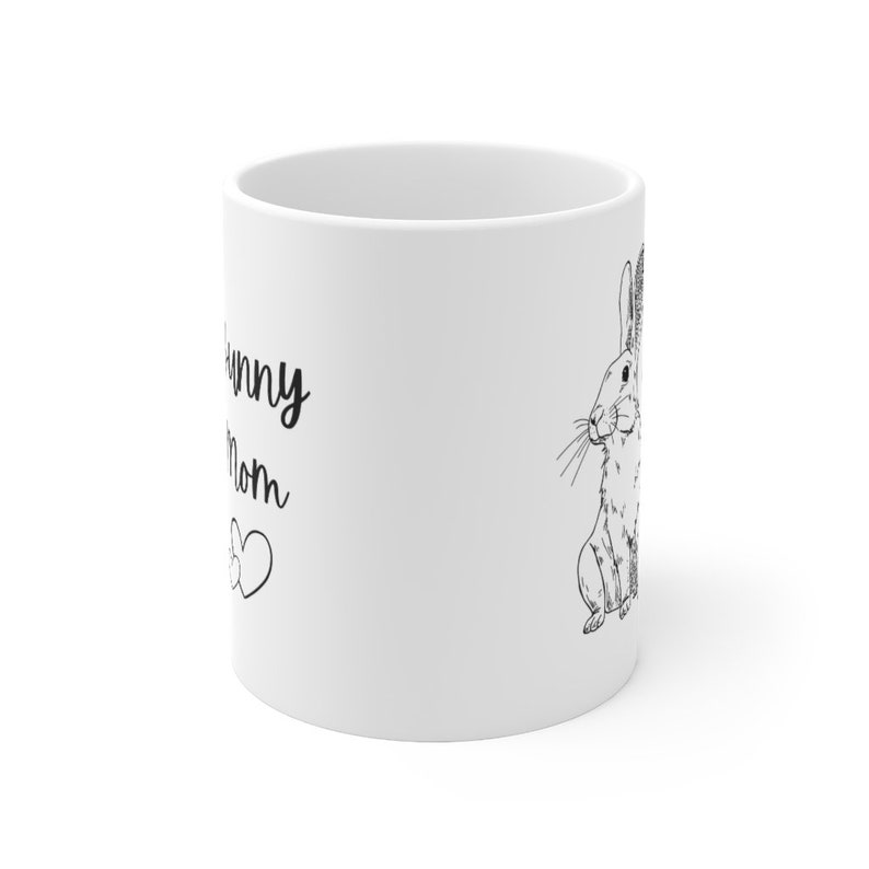 White ceramic mug with black design of rabbit that says "bunny mom" with two hearts.  Photo shows the side opposite of the handle to show that the mug has the design printed on both sides.