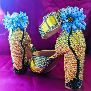 May include: A pair of high-heeled sandals with yellow straps and blue flower embellishments. The heels are covered in colourful rhinestones.