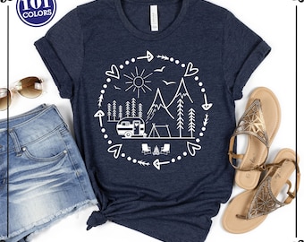 May include: A dark navy blue short-sleeve t-shirt featuring a white circular graphic print of a camping scene with a camper, tent, mountains, trees, sun, and birds. The design is enclosed by a dotted border with arrows and heart shapes.