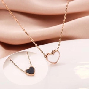May include: A delicate gold chain necklace with a small heart pendant. The heart is white with a gold border and is slightly raised. The chain is thin and delicate.