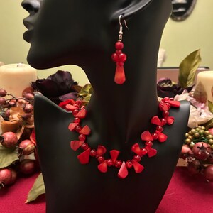 May include: A red beaded necklace and matching earrings. The necklace is made of red beads and has a teardrop shape. The earrings are also made of red beads and have a teardrop shape.