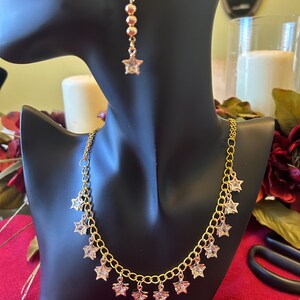 May include: Gold necklace and earrings set with star-shaped charms. The necklace has a chain with multiple star-shaped pendants. The earrings are drop earrings with a star-shaped charm at the end.