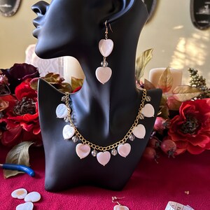May include: A white heart-shaped necklace and earrings set with gold chain and clear crystal accents. The necklace has multiple heart-shaped pendants and the earrings are dangle style.