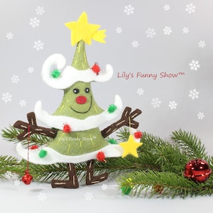 K&ouml;nnte beinhalten: Ein gr&uuml;ner Filz-Weihnachtsbaum mit wei&szlig;em Filzbesatz und einem gelben Stern oben. Der Baum hat ein l&auml;chelndes Gesicht und braune Filz-Arme und -Beine. Der Baum ist mit roten und gr&uuml;nen Filz-Ornamenten geschm&uuml;ckt. Der Baum steht auf einem gr&uuml;nen Kiefern-Zweig mit einem roten Glocken-Anh&auml;nger.