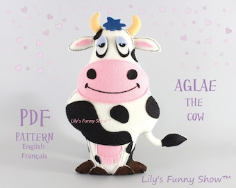 May include: A PDF pattern for sewing a plush toy cow named Aglae. The cow is white with black spots and has a pink nose and hooves. The pattern is available in English and French.