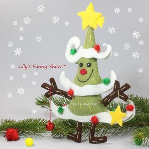 K&ouml;nnte beinhalten: Ein gr&uuml;ner Filz-Weihnachtsbaum mit einem wei&szlig;en Filzhut und einem gelben Stern oben. Der Baum hat ein l&auml;chelndes Gesicht und rote Bommeln als Dekoration. Der Baum steht auf einem gr&uuml;nen Zweig mit einer roten Bommel und einem gelben Stern, der daran h&auml;ngt. Der Text "Lily's Funny Show&trade;" ist auf dem Baum und dem Zweig zu sehen.