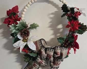 May include: A Christmas wreath with a wooden bead base, adorned with red poinsettias, white flowers, green holly leaves, pinecones, and a plaid ribbon with "Merry Christmas" text. The wreath is hanging on a white wall.