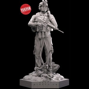 May include: A grey, detailed figurine of a soldier holding a rifle, standing on a base with the words "DEATH STRANDING" inscribed on it.
