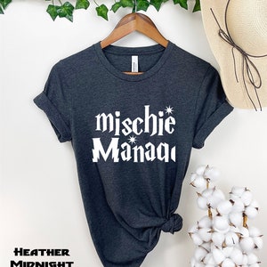May include: A dark heather grey t-shirt with the text "mischie* Manaqi" in white lettering. The shirt is tied in a knot at the bottom.