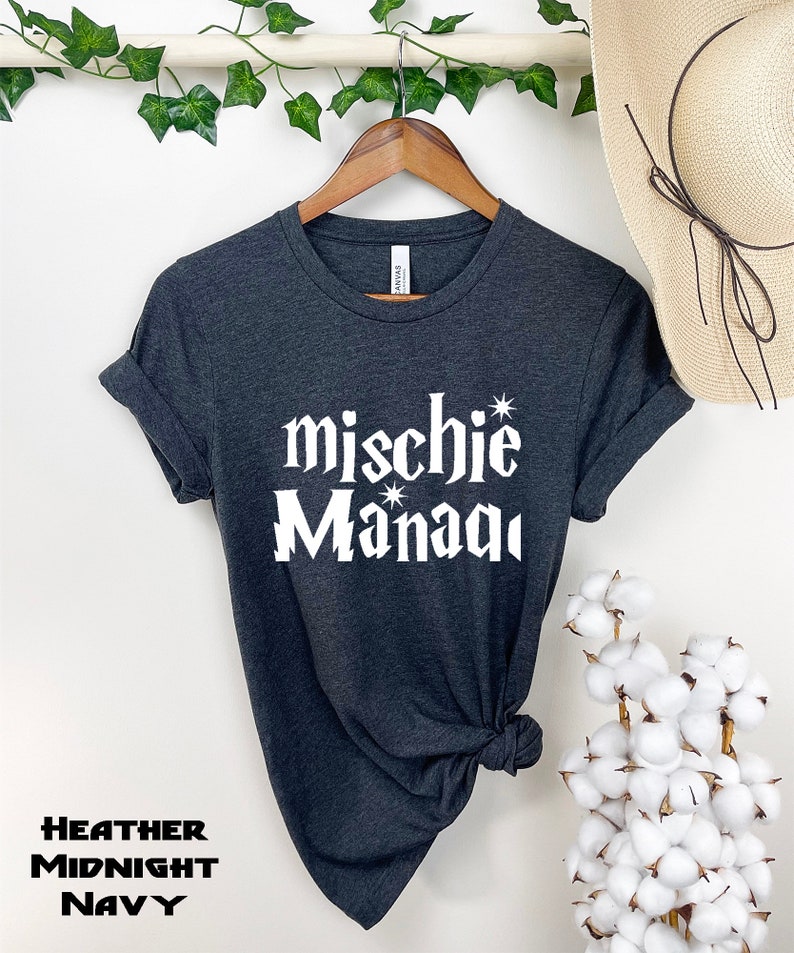 May include: A dark heather grey t-shirt with the text "mischie* Manaqi" in white lettering. The shirt is tied in a knot at the bottom.