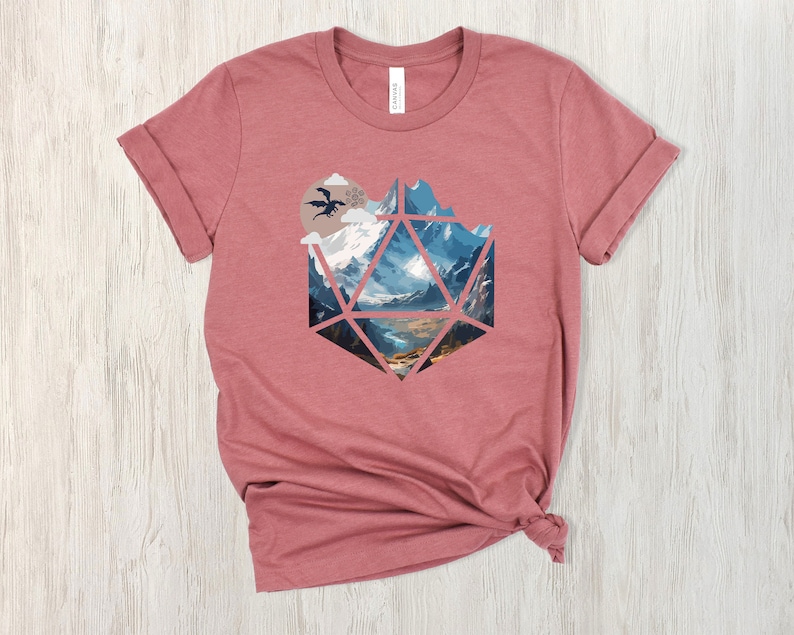 Pode incluir: Uma camiseta marrom-avermelhada com um gr&aacute;fico de uma paisagem montanhosa dentro de uma forma geom&eacute;trica que se assemelha a um dado de vinte lados. Um drag&atilde;o preto voa no c&eacute;u acima das montanhas.