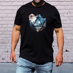 Pode incluir: Uma camiseta preta com um gr&aacute;fico de uma paisagem montanhosa dentro de uma forma geom&eacute;trica, que se assemelha a um dado. O gr&aacute;fico apresenta uma lua e dois drag&otilde;es voando.