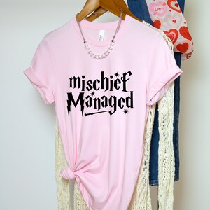 May include: Pink t-shirt with black text that reads "mischief managed" with a lightning bolt and wand graphic.
