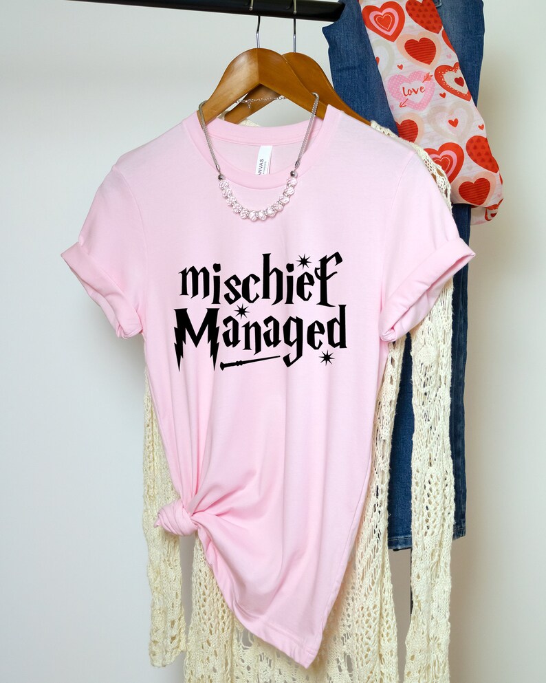 May include: Pink t-shirt with black text that reads "mischief managed" with a lightning bolt and wand graphic.