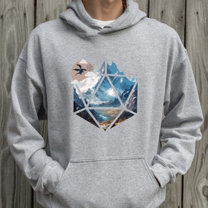 Pode incluir: Uma camisa de moletom cinza com capuz com uma estampa gr&aacute;fica de uma paisagem montanhosa dentro de uma forma geom&eacute;trica que se assemelha a um dado de vinte lados. Uma silhueta preta de um drag&atilde;o voa sobre as montanhas.