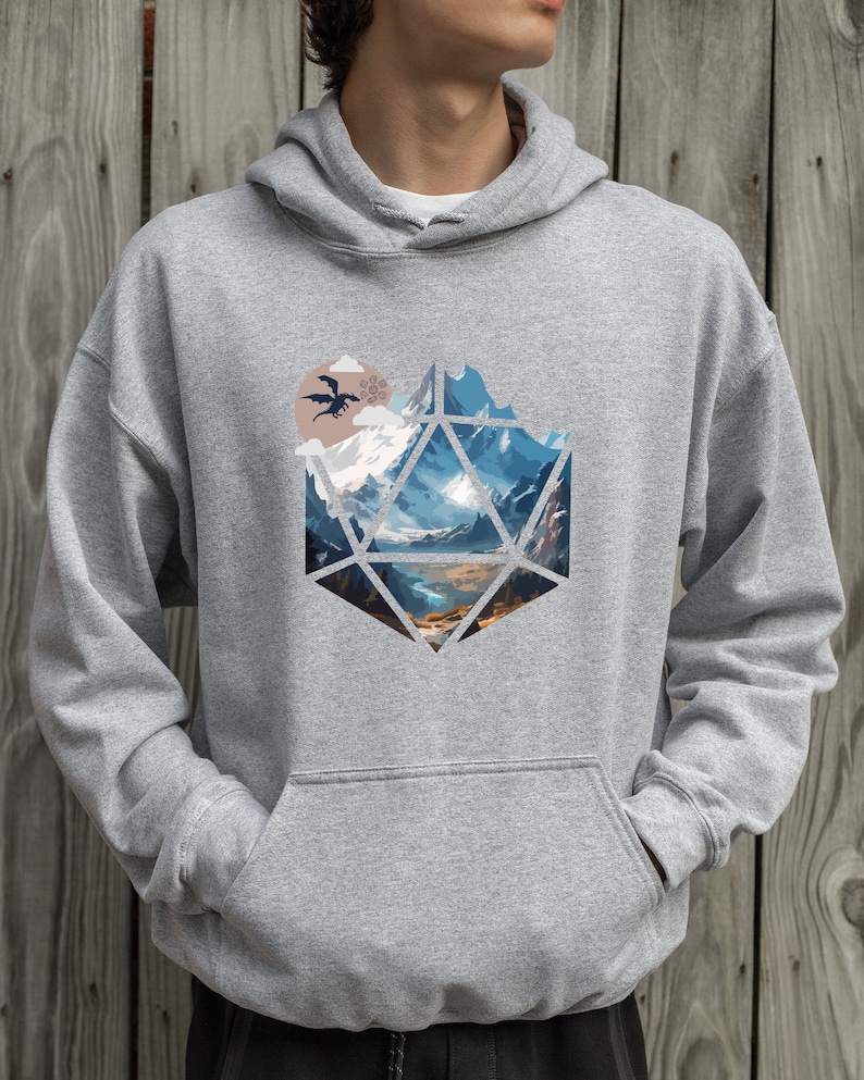 Pode incluir: Uma camisa de moletom cinza com capuz com uma estampa gr&aacute;fica de uma paisagem montanhosa dentro de uma forma geom&eacute;trica que se assemelha a um dado de vinte lados. Uma silhueta preta de um drag&atilde;o voa sobre as montanhas.