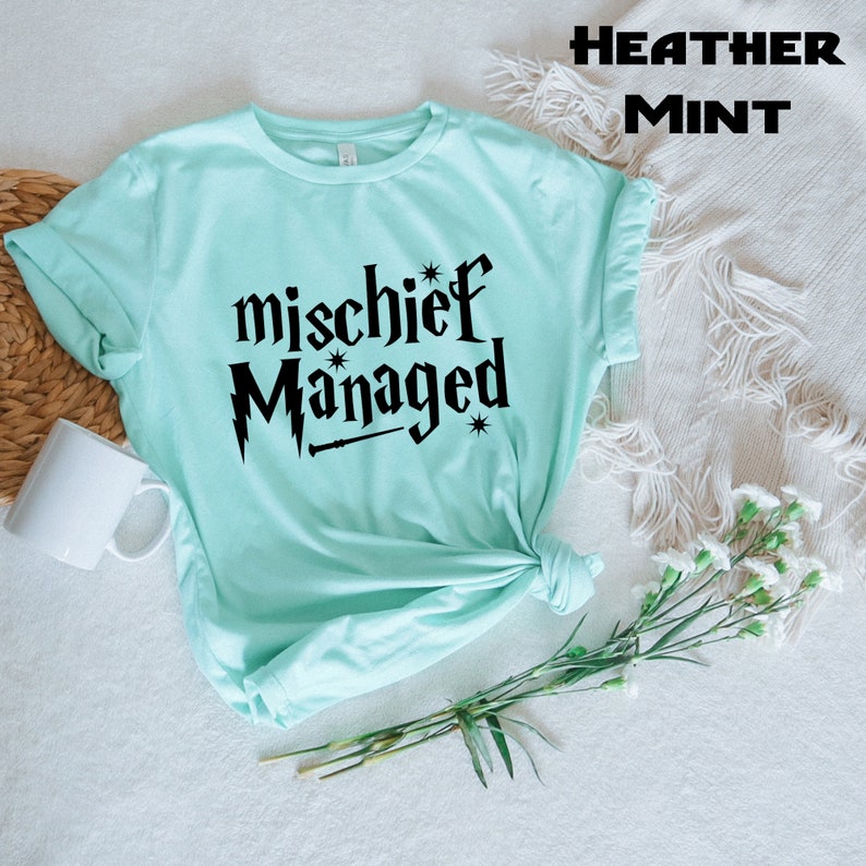 May include: A light blue t-shirt with the text "mischief managed" in black lettering. The text is stylized to look like a Harry Potter inspired design.