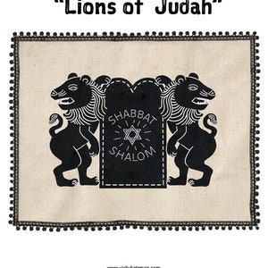 May include: DIY Challah Cover with the text "Lions of Judah". The cover features a beige background with a black border and black lion illustrations. The lions flank a black sign with the words "Shabbat Shalom" and a Star of David.