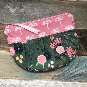 May include: A half-circle zippered pouch with a pink floral print on the top half and a green floral print on the bottom half.