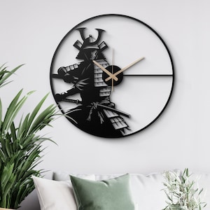 Op de afbeelding: Zwarte en witte wandklok met een silhouet van een samoerai-krijger. De klok heeft een ronde, zwarte metalen frame en gouden wijzers.