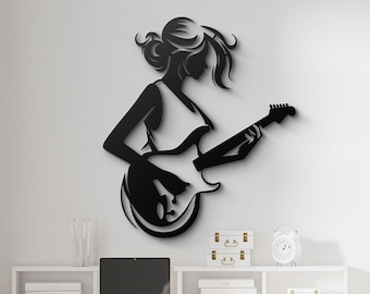 May include: Black silhouette wall art of a woman playing an electric guitar. The art is mounted on a white wall above a white desk with a white chair.