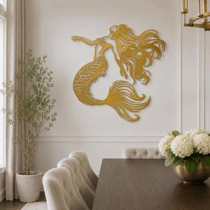 Puede incluir: Una pieza de arte mural de metal en color dorado que representa a una sirena con cabello largo y fluido y una cola detallada. La silueta muestra a la sirena en una pose de nado con los brazos extendidos hacia arriba y detalles recortados.