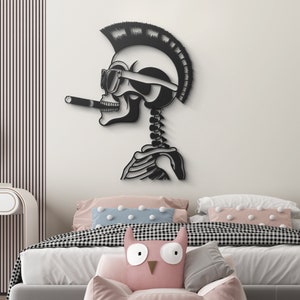 May include: Black and white wall decor featuring a skeleton with a mohawk, sunglasses, and a cigarette. The skeleton is in a relaxed pose with its arms crossed. The decor is mounted on a white wall above a bed with pink and blue pillows.