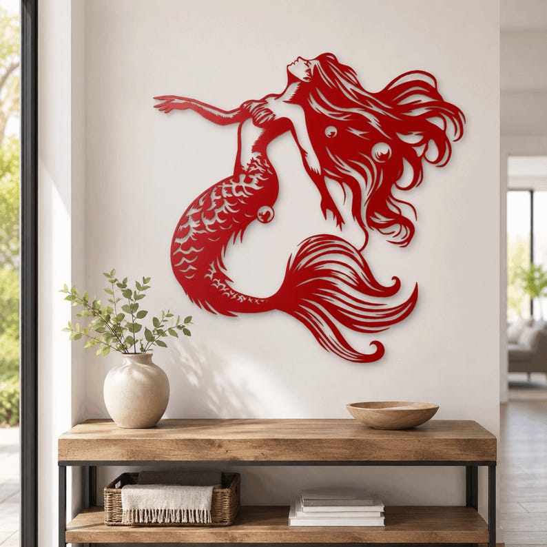 Puede incluir: Una pieza de arte mural de metal rojo que presenta la silueta estilizada de una sirena con cabello largo y fluido, espalda arqueada y un dise&ntilde;o de cola intrincado. La obra recortada muestra una pose din&aacute;mica con un brazo extendido.