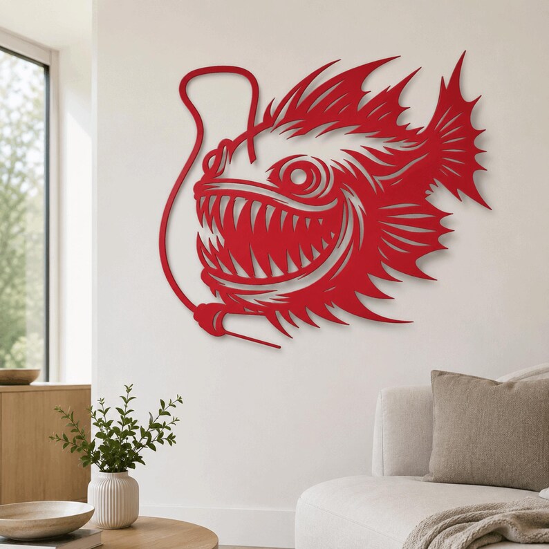 May include: A red wall art piece shaped like an anglerfish with a prominent lure, sharp teeth, and spiky fins. The design features a cutout silhouette style with intricate lines defining the fish's features, mounted flat against a plain wall.