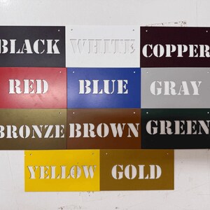 May include: A collection of eleven rectangular metal signs arranged in a grid, each featuring a cutout word identifying its color: Black, White, Copper, Red, Blue, Gray, Bronze, Brown, Green, Yellow, and Gold. Each sign has two small holes.