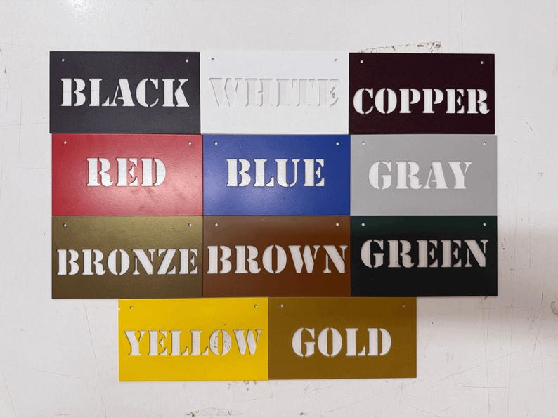 May include: A collection of eleven rectangular metal signs arranged in a grid, each featuring a cutout word identifying its color: Black, White, Copper, Red, Blue, Gray, Bronze, Brown, Green, Yellow, and Gold. Each sign has two small holes.